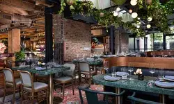 A restaurant interior with tables set for dining, featuring hanging plants and brick accents