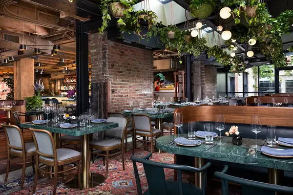 A restaurant interior with tables set for dining, featuring hanging plants and brick accents