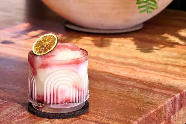 A frozen beverage served in a decorative glass, garnished with a dried lime slice, on a wooden surface