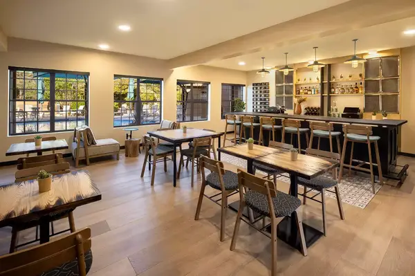 A modern café space with tables, chairs, and a bar area, well-lit with natural light from large windows