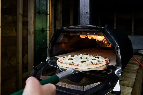 A pizza on a pizza peel being inserted into an outdoor pizza oven