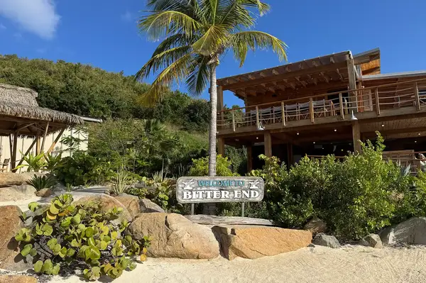 A beachfront scene featuring the Bitter End Yacht Club with a sign and tropical foliage