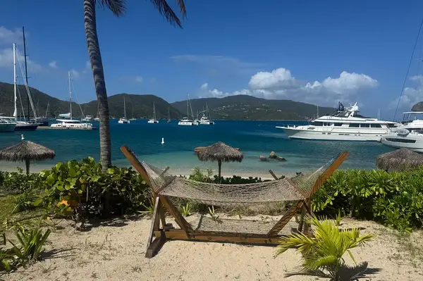 Hammock on a sand beach with yachts and mountains in the distance, view of Bitter End Yacht Club
