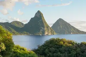 A view of the twin Pitons across a calm ocean inlet with lush greenery in the foreground
