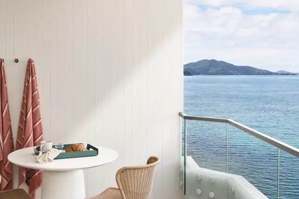 A table with chairs and a tray, towels hanging on a wall, balcony with sea view in the background