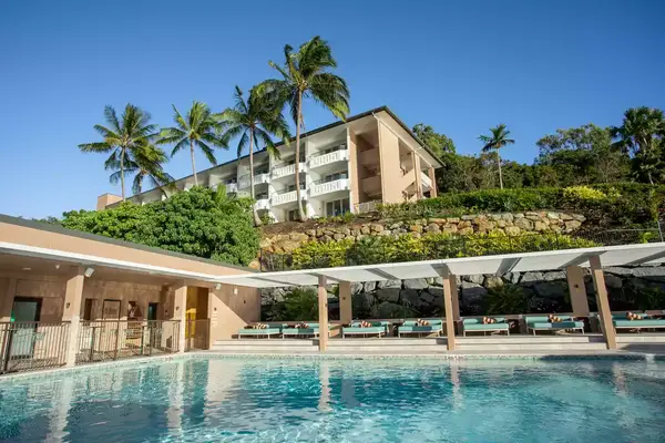 A hotel exterior with a terrace, pool area, and palm trees in the background