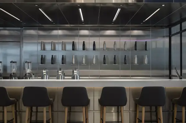 A modern bar with stools and a wall lined with bottles and metallic surfaces