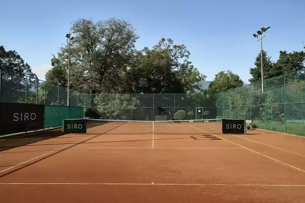Tennis court with SIRO branding, surrounded by fences and greenery, under clear skies