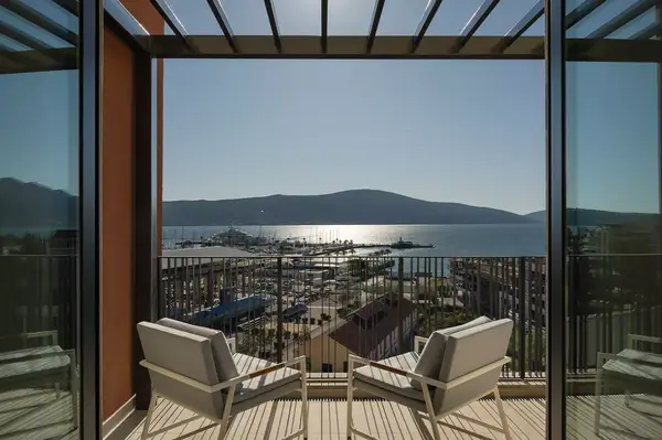 View from a balcony with lounge chairs overlooking a harbor and mountains