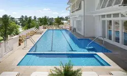Outdoor swimming pool at a resort with a view of trees and a white building with large windows
