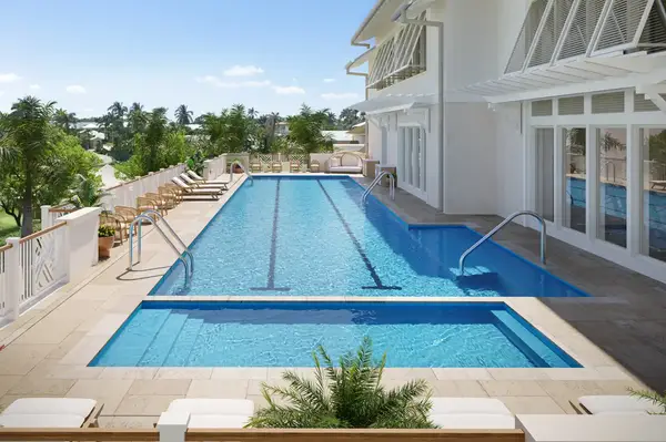 Outdoor swimming pool at a resort with a view of trees and a white building with large windows