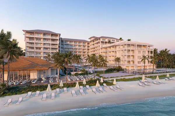 Exterior view of a beachfront resort with multiple buildings, palm trees, and lounge chairs on the beach