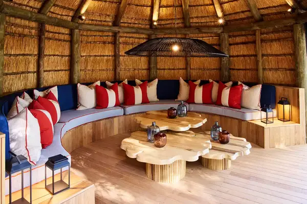A circular seating area with cushions and wooden tables under a thatched roof in a tropical lodge