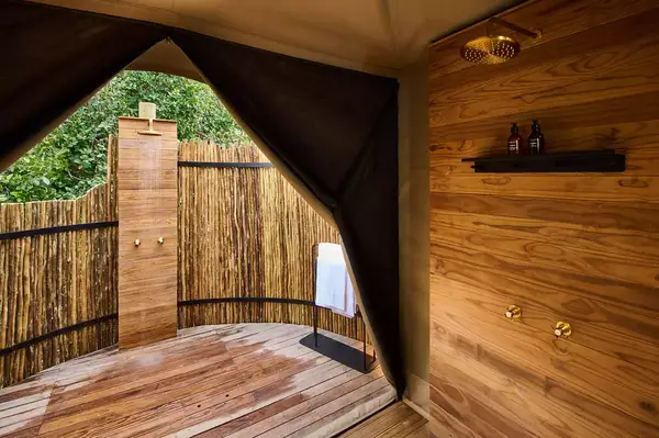 Open-air bathroom with wood paneling and a view of a tree-surrounded outdoor shower area