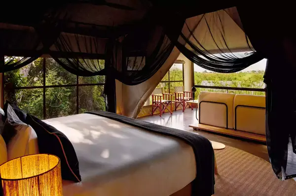 Lodge bedroom with canopy bed, view of outdoor seating and greenery through large windows