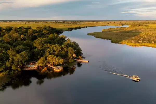 Lodge by a river, surrounded by lush landscape, a boat moving in the water