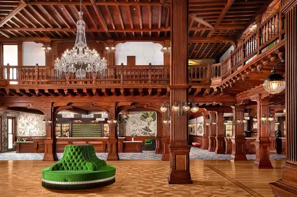 Grand hotel lobby with intricate woodwork, a chandelier, and a green tufted seating area center
