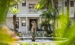 A statue in a fountain surrounded by greenery in a garden setting with a building in the background
