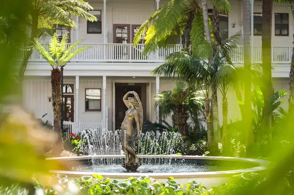 A statue in a fountain surrounded by greenery in a garden setting with a building in the background