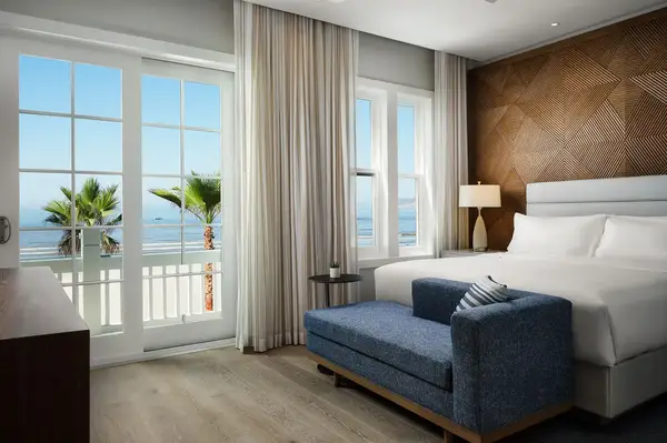Hotel room with a bed, a sofa, and large windows with a view of palm trees and the ocean