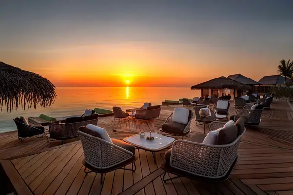 Outdoor lounge and dining area with ocean view at sunset 