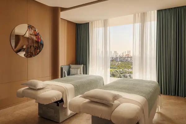Spa room with two treatment tables and a large window overlooking a city view
