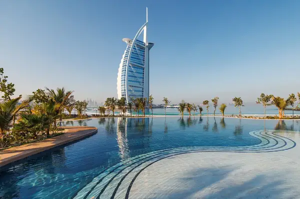 A luxury hotel by the sea viewed from a pool surrounded by palm trees