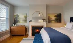 A guestroom with a fireplace, bed, bench, and dresser setup