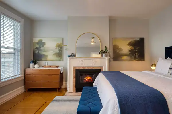 A guestroom with a fireplace, bed, bench, and dresser setup