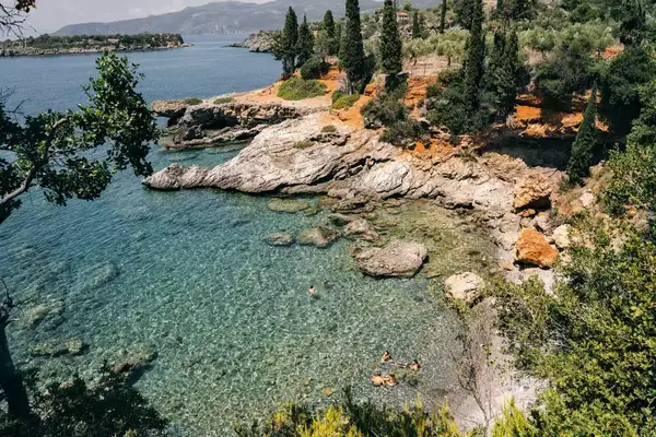 A hidden cove in Kardamyli, Greece, surrounded by greenery. Four people are shown in the water
