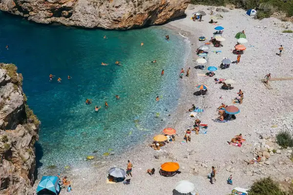 A small rocky beach in Kardamyli, Greece, with sunbathers, colorful umbrellas, and turquoise water