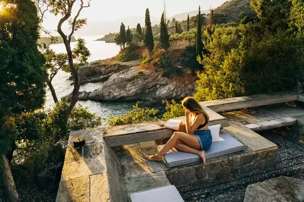 A woman reads a book on the terrace of a home in Kardamyli, Greece, overlooking the sea
