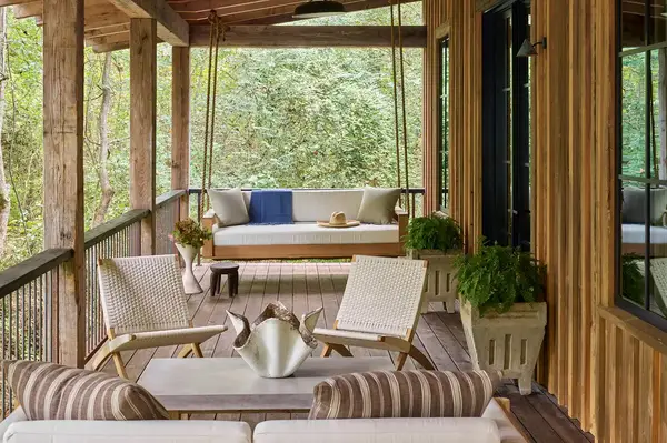 A wooden porch with seating a swing and greenery around