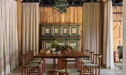 Dining area with a wooden table chairs curtains and a decorative cabinet in a rustic setting