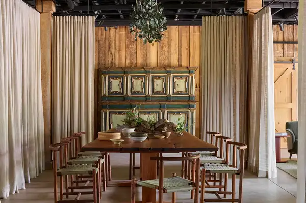 Dining area with a wooden table chairs curtains and a decorative cabinet in a rustic setting