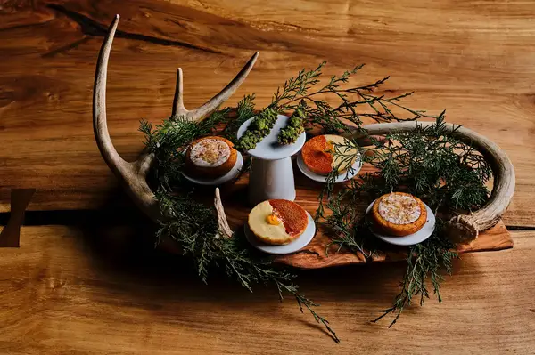 A wooden platter with decorative greenery antlers and assorted small pastries arranged neatly