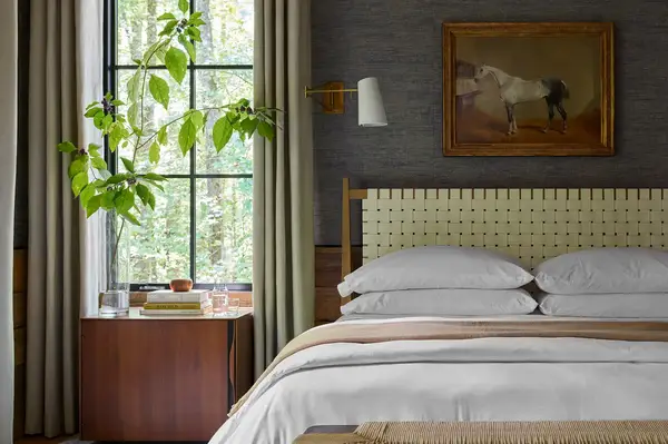 Interior of a cozy bedroom featuring a bed nightstand window plant and a painting of a horse on the wall