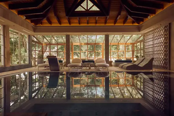 Indoor spa with lounge chairs by a pool, surrounded by glass walls and decorated wooden ceiling