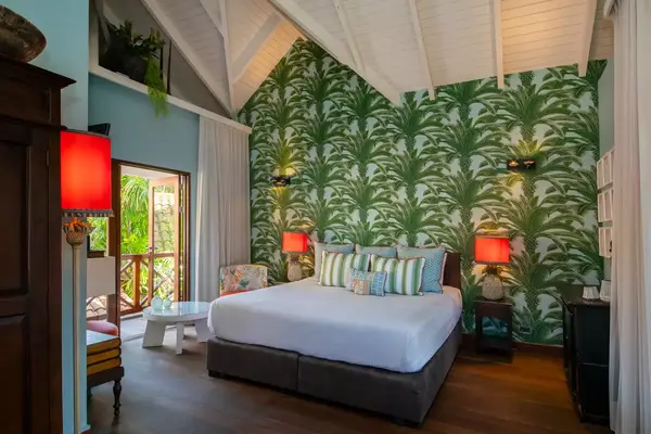 A decorated hotel room with a tropical leaf wallpaper, a large bed, and accent lighting