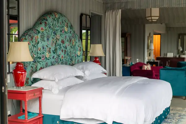 A well-furnished bedroom with a patterned headboard, two side tables with lamps, and white bedding