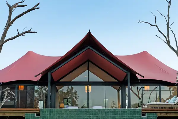 Modern building with a tent-like roof and glass facade, surrounded by a natural landscape