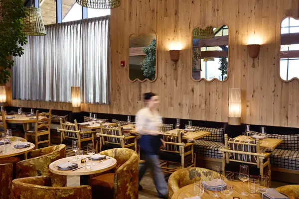 A cozy restaurant interior with wooden furniture and decorative wall mirrors a person walking in motion
