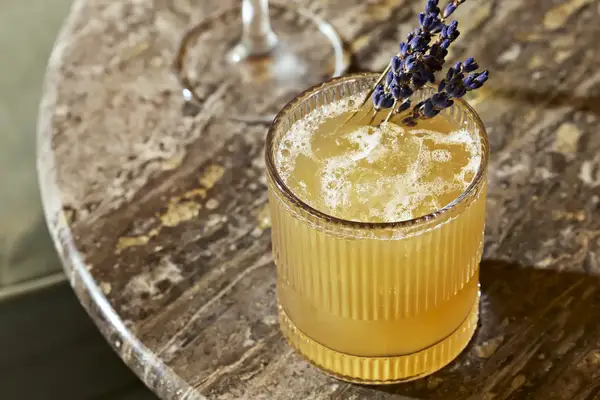 A cocktail garnished with lavender on a marble table