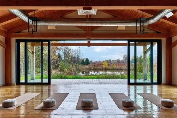 Large yoga studio with mats and cushions open sliding doors revealing a serene garden and pond view outside