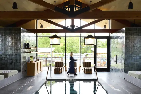 An indoor spa pool area with a person walking in front of large windows