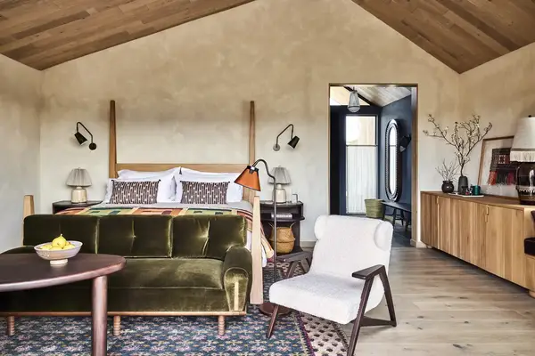 A bedroom interior featuring a bed with pillows and a blanket a green sofa an armchair and a wooden sideboard under slanted ceilings