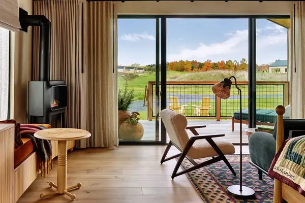 Cozy interior of a cottage with a view of a meadow through large windows and outdoor seating on a patio