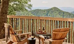Two wooden chairs on a deck overlooking a scenic hilly landscape with items on a small table between them