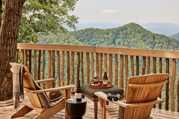 Two wooden chairs on a deck overlooking a scenic hilly landscape with items on a small table between them