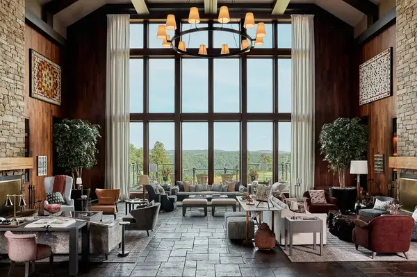 Spacious hall with large windows sofas tables and a chandelier overlooking outdoor greenery